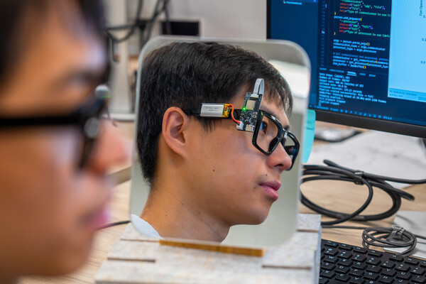 Dongyin Hu models BlinkWise glasses at his computer station.