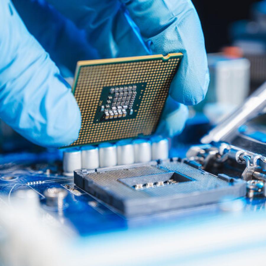 A computer chip being placed by a rubber-gloved hand.
