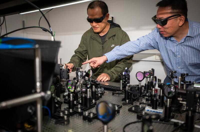 Tianwei Wu (left) and Liang Feng (right) demonstrating some of the apparatus used to develop the new, light-powered chip.