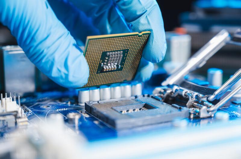 A computer chip being placed by a rubber-gloved hand.
